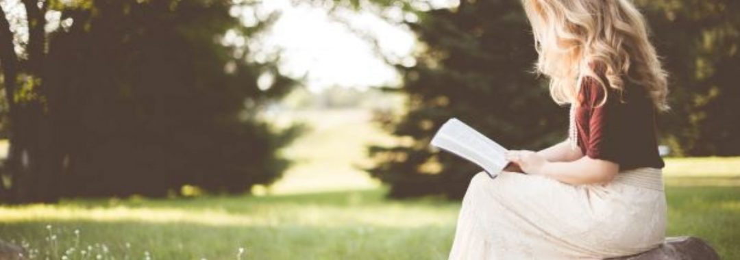 Little-girl-sitting-down-on-a-log-reading-a-book.