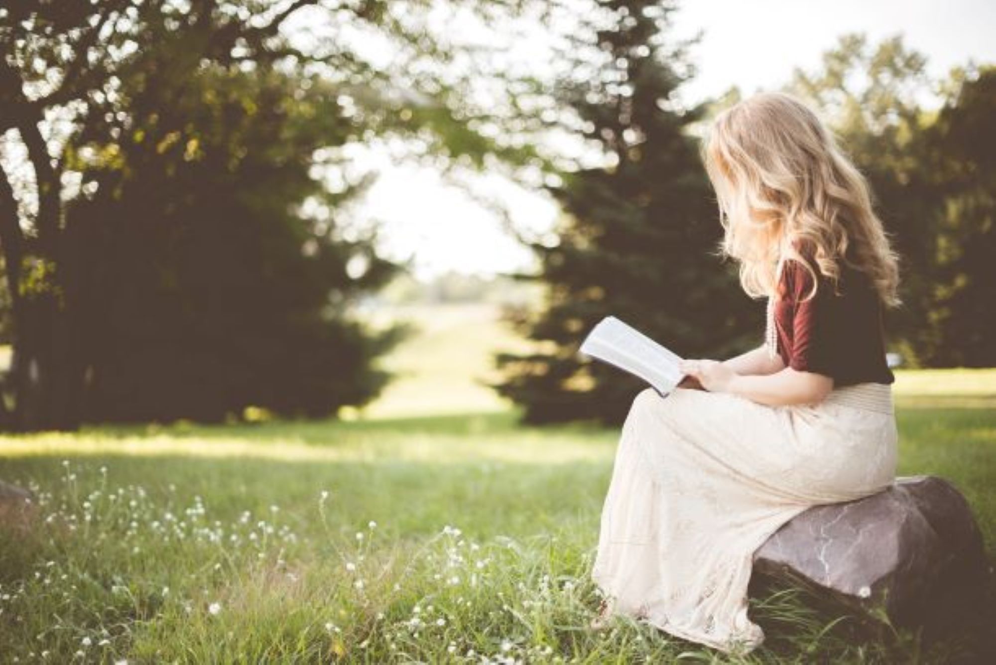 Little-girl-sitting-down-on-a-log-reading-a-book.